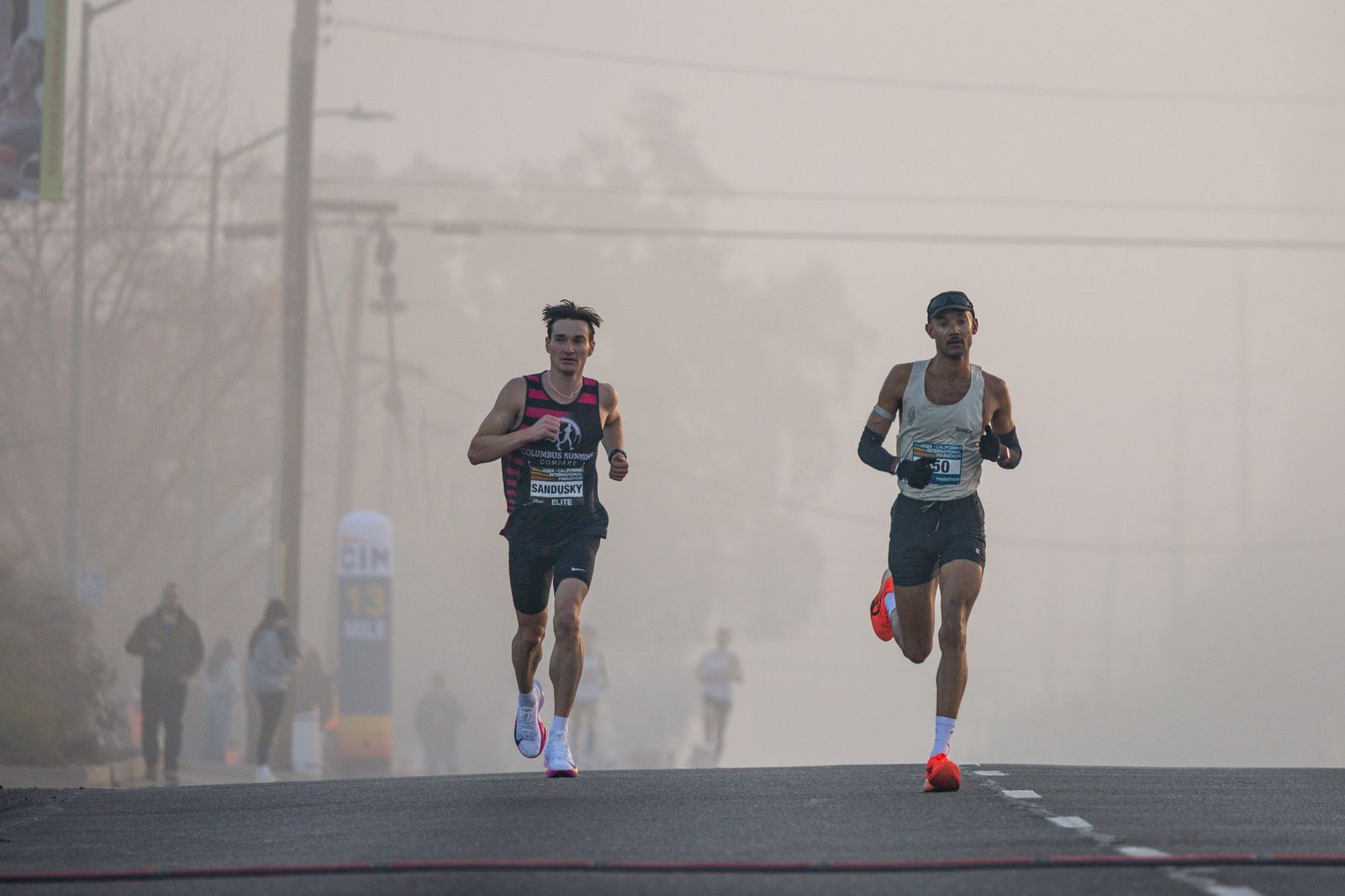 Deux coureurs en tête d'une course sur route dans la brume matinale, au coude à coude